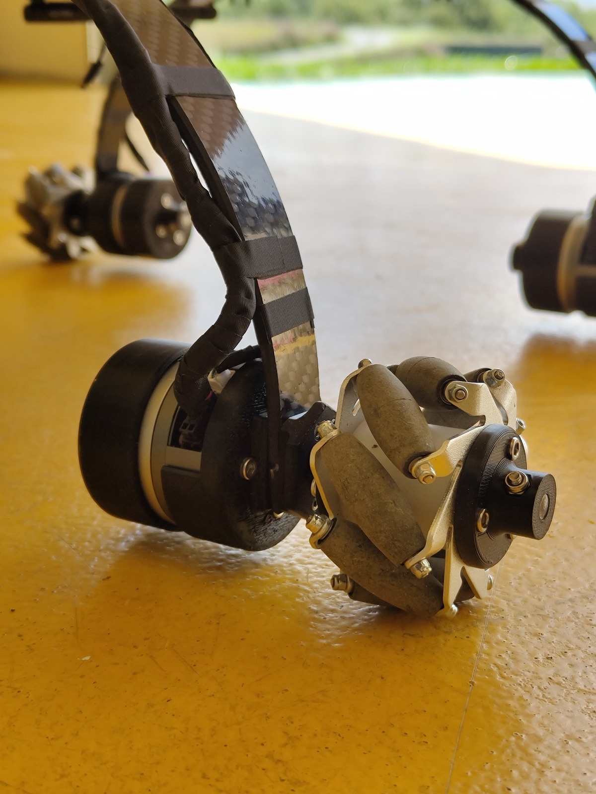 Close view of one wheeled landing leg of the proof of concept, a carbon leg ending in a driven omnidirectional wheel.